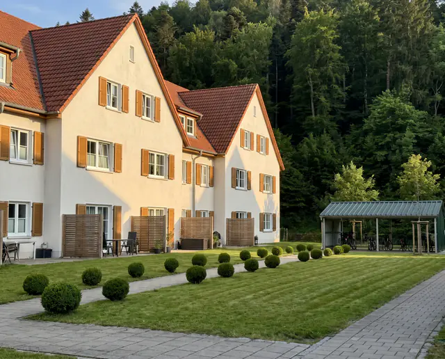 Visualisierung: Wohnanlage am Ortsrand von Gundelfingen mit gemähtem Rasen, Buchskugeln entlang des Weges und Fahrradunterstand, dahinter bewaldete Schwarzwaldhänge