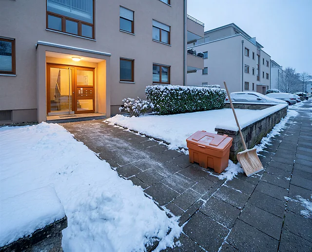 Visualisierung: geräumter und gestreuter Weg zum Hauseingang einer Wohnanlage, daneben Streugutkiste und Schneeschieber